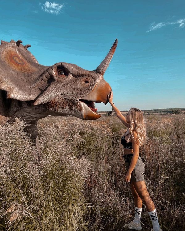 Life size dinosaur replicas standing in tall grass at an abandoned park
